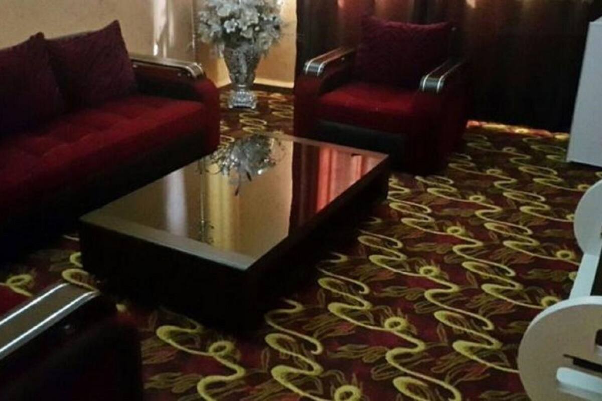 Una habitación de hotel con un sofá rojo, una mesa de centro de vidrio y una alfombra estampada.