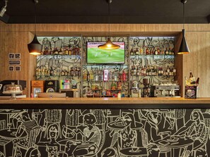 A bar area with a television, shelves of bottles, and a counter with a coffee machine. - ibis Cali Granada (Cali)