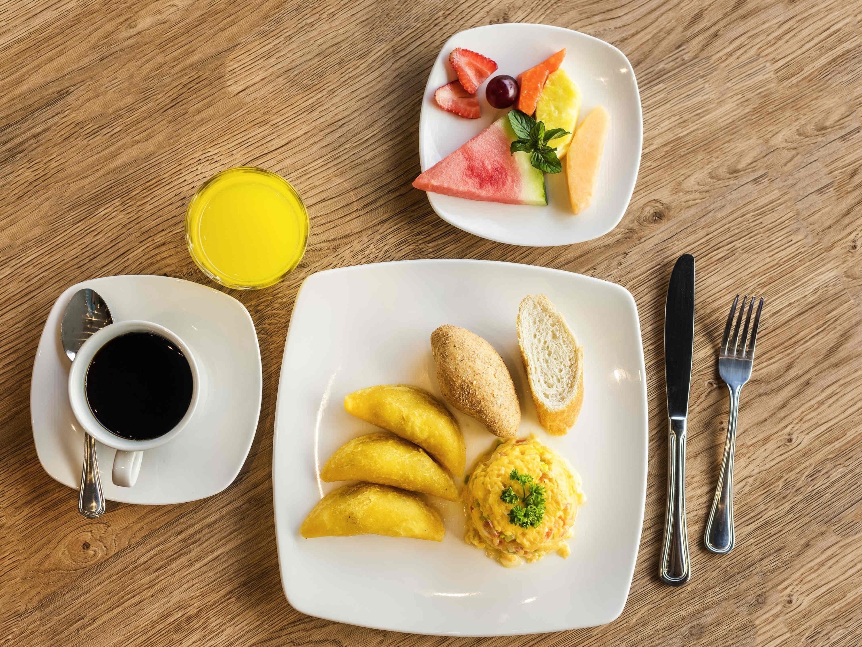 A breakfast setting with a plate of food, a cup of coffee, and a glass of juice on a wooden table.