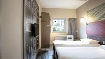 Habitación de hotel con dos camas, un escritorio, un televisor y una ventana con cortinas.