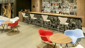 Un área de bar moderna con mostrador de madera, sillas coloridas y un mural blanco y negro en la pared.