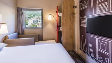 Habitación de hotel con cama, escritorio, silla, televisor y ventana con vista a la ciudad.