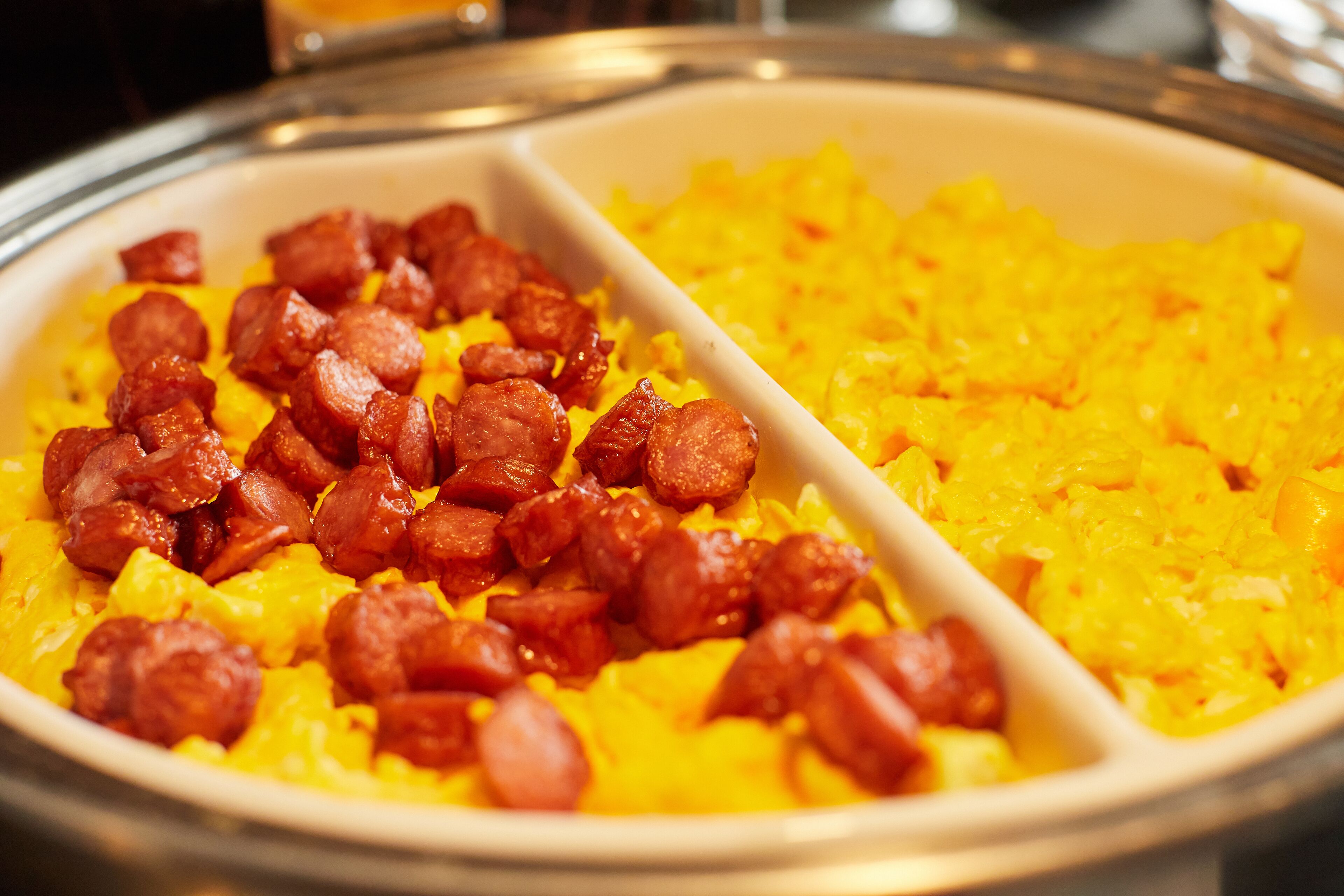 A buffet with two sections: one with yellow rice and another with sausage.