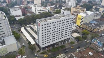 Um hotel com vários andares e uma fachada com grade de janelas, cercado por edifícios urbanos e ruas.