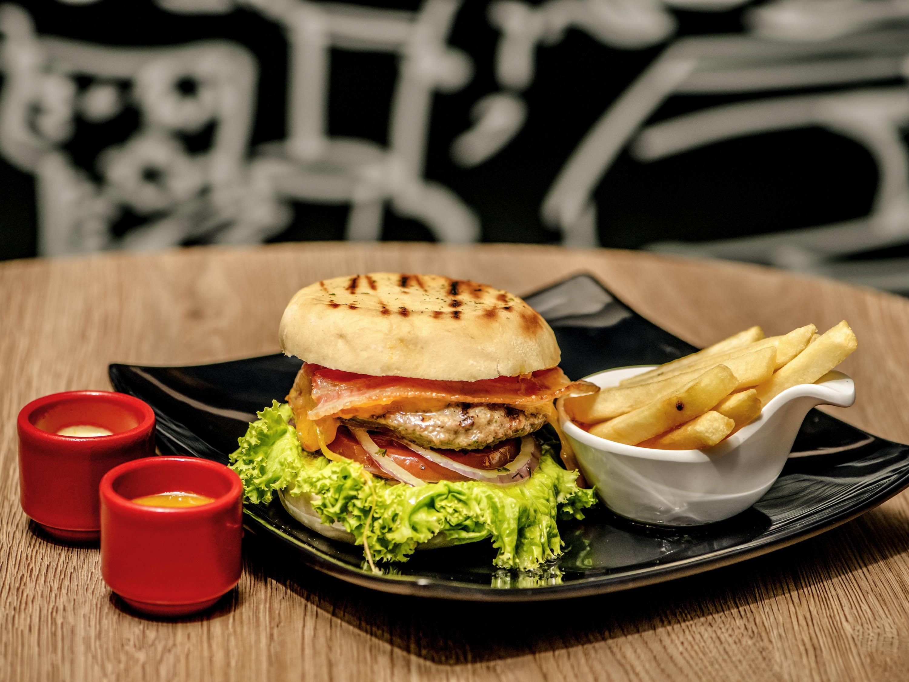 A burger with fries on a plate, two red cups, and a black table.