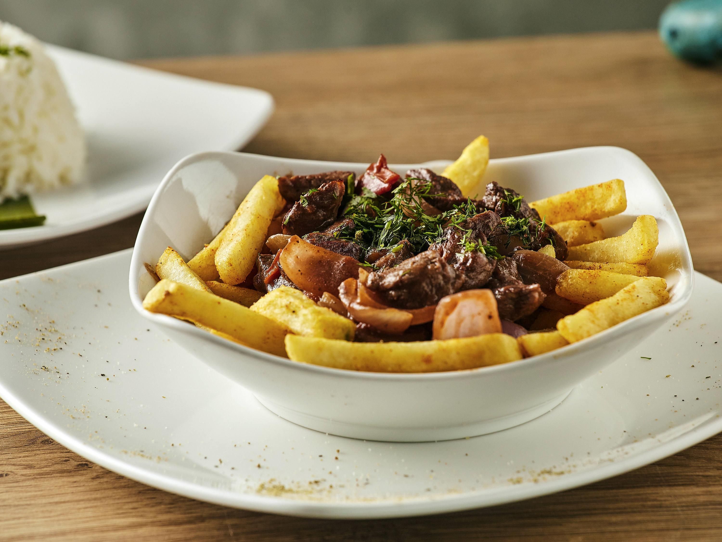 A white bowl of beef stew with fries on a white plate.