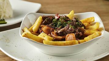 Un tazón blanco de estofado de carne con papas fritas sobre un plato blanco.