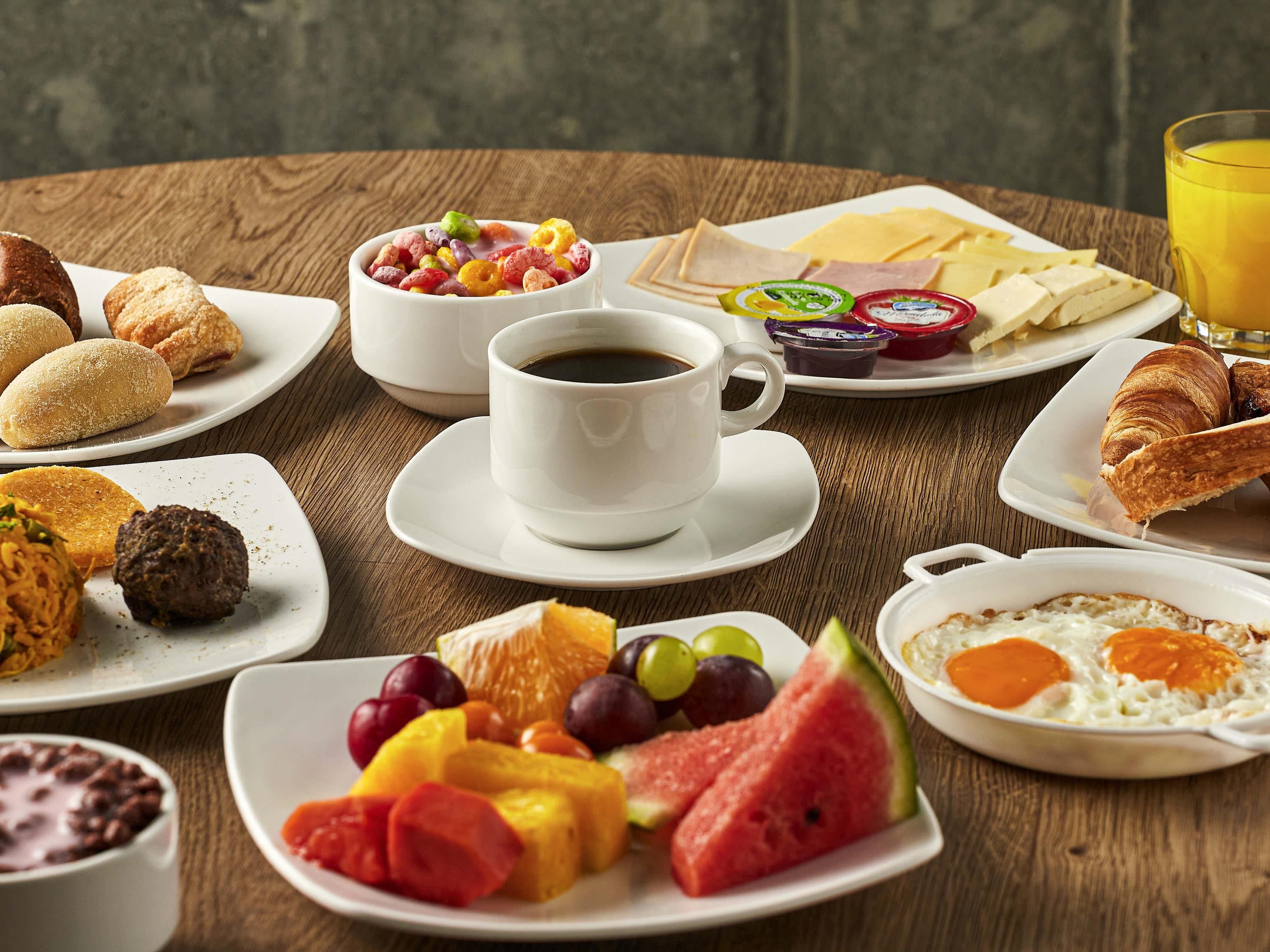 A breakfast table with various food items, a cup of coffee, and a glass of orange juice.