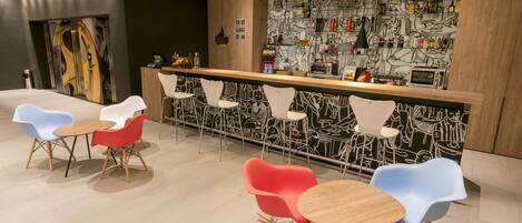 Un bar moderno con mostrador de madera, sillas coloridas y una pared con ilustraciones en blanco y negro.