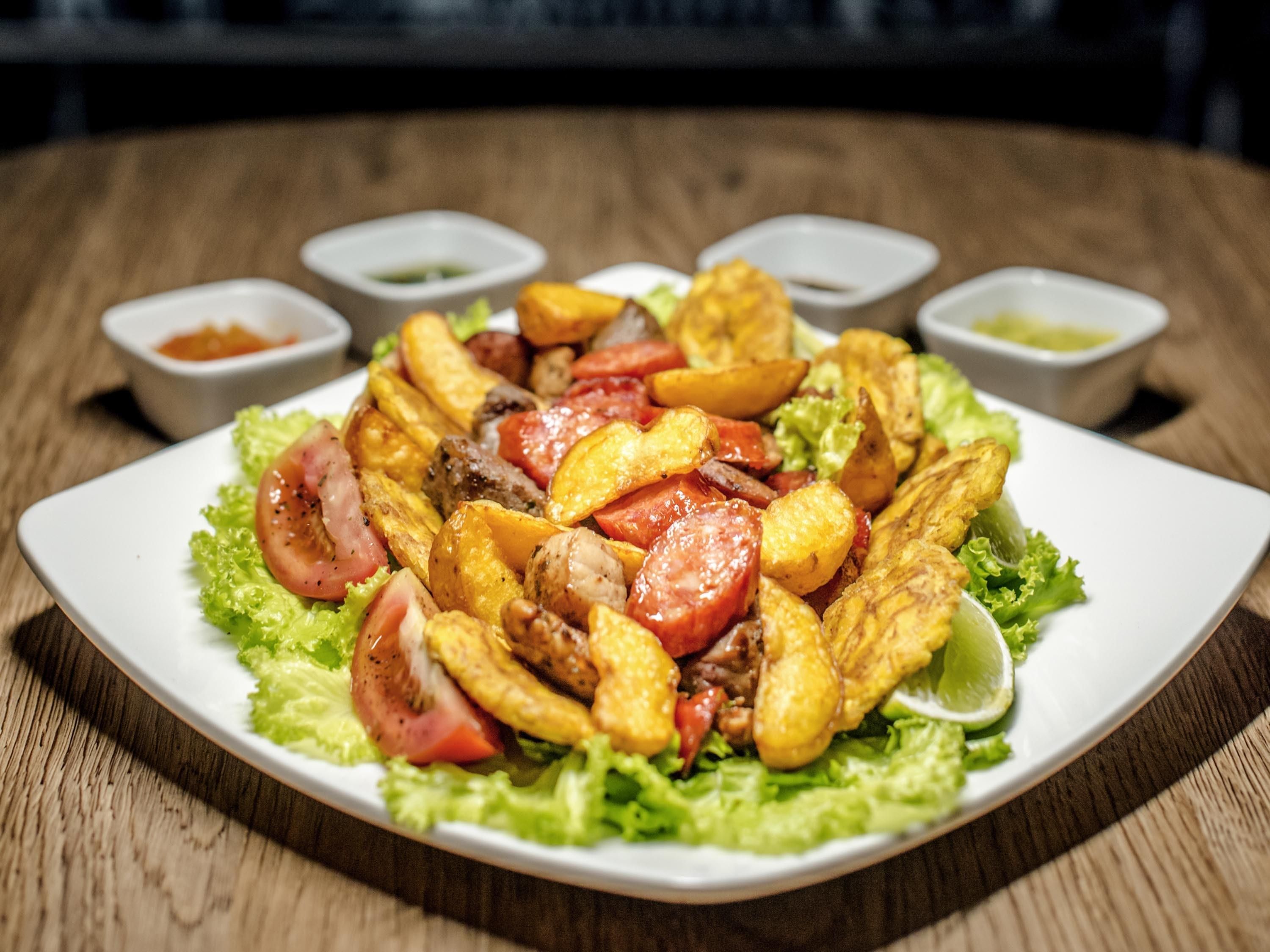 Un plato de comida con papas fritas, carne y verduras, acompañado de recipientes pequeños con salsas.