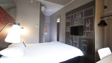 A hotel room with a bed, a desk, a chair, a lamp, and a wall with chalkboard-style drawings.