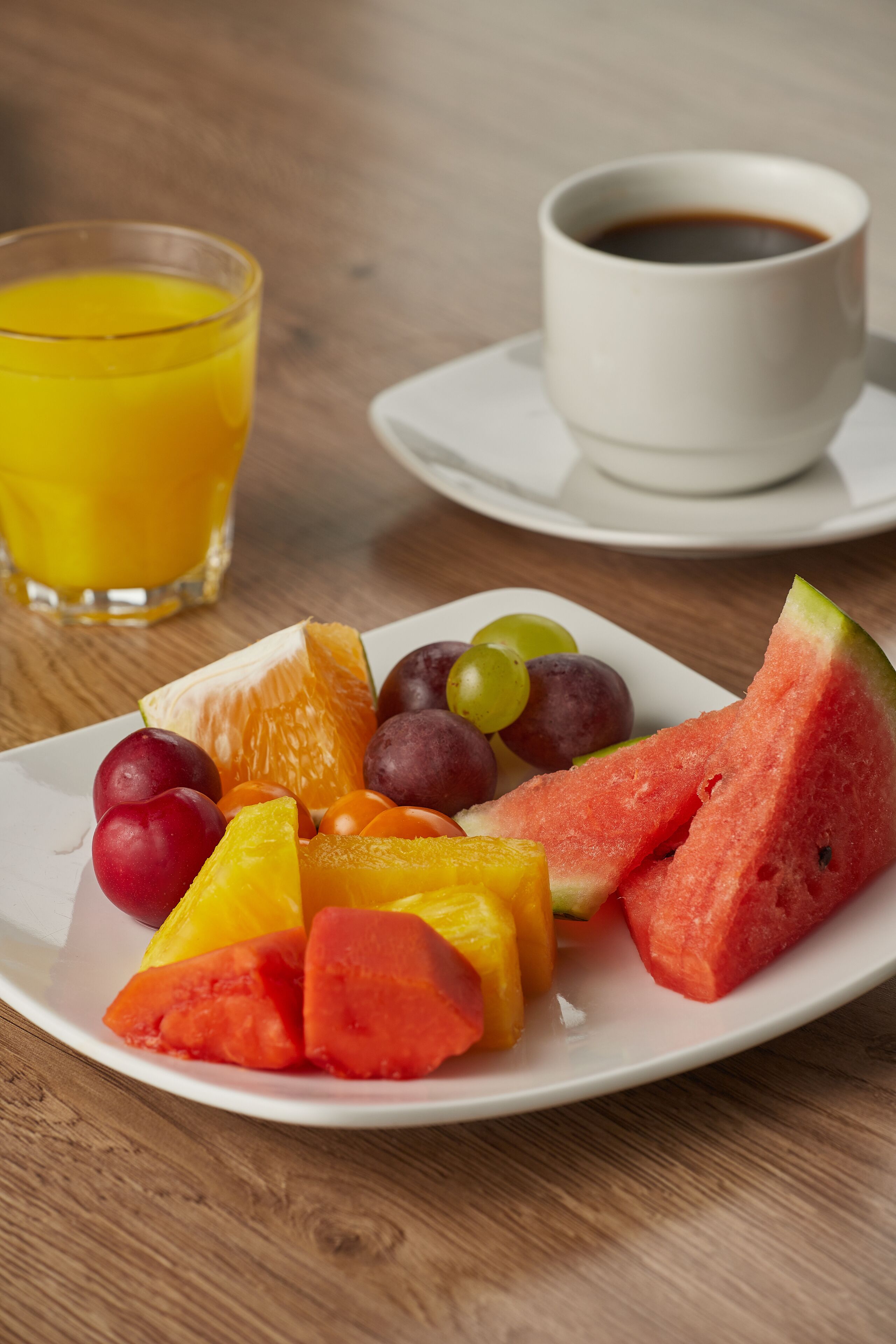 A plate of fruit and a cup of coffee on a wooden table.