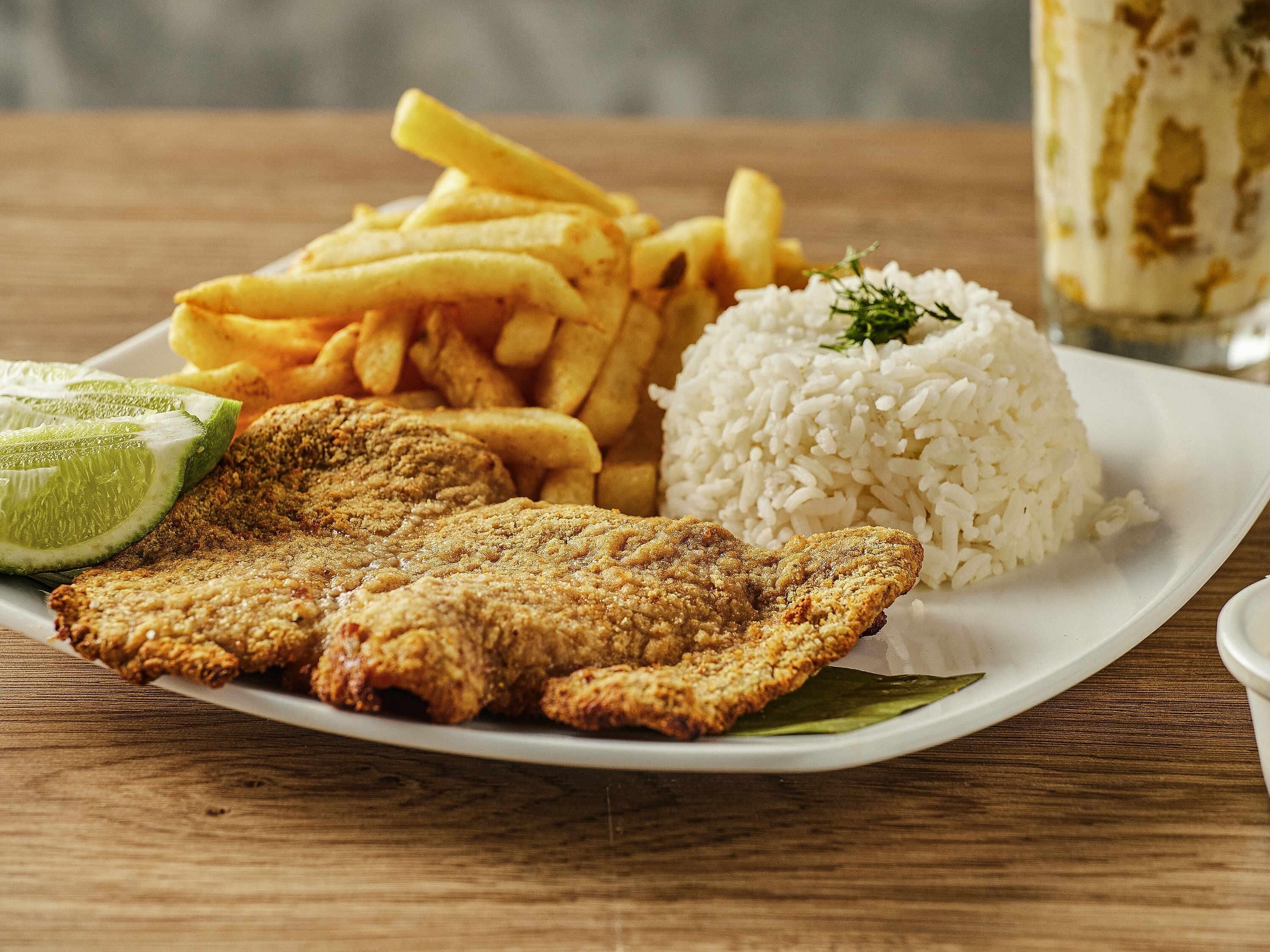 Une assiette de poisson frit, de frites, de riz et de tranches de citron vert.