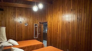 Una habitación con paneles de madera, dos camas con ropa de cama blanca y naranja, y una lámpara en el techo.