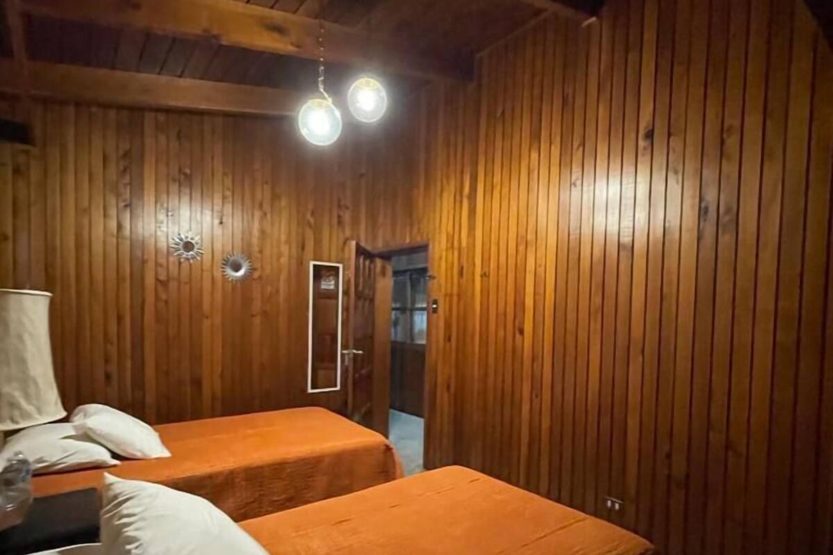 Una habitación con paneles de madera, dos camas con ropa de cama blanca y naranja, y una lámpara en el techo.