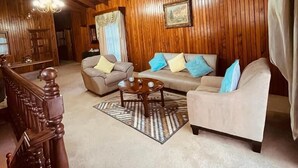 Un salón acogedor con paredes de madera y techo alto, que incluye un conjunto de sofás, una mesa de centro y una escalera con barandilla de madera.