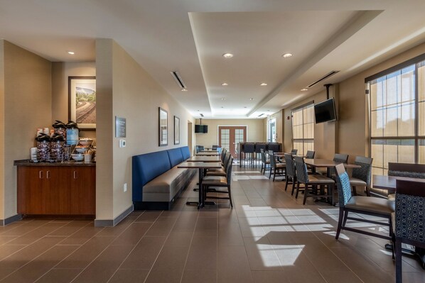 Une salle à manger d’hôtel spacieuse, avec de longues tables et des bancs, un coin cuisine et un téléviseur fixé au mur.