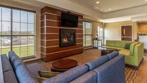 A spacious lobby with a fireplace, a flat-screen TV, and a green sofa. - Comfort Inn & Suites – Harrisburg Airport – Hershey South (Middletown)