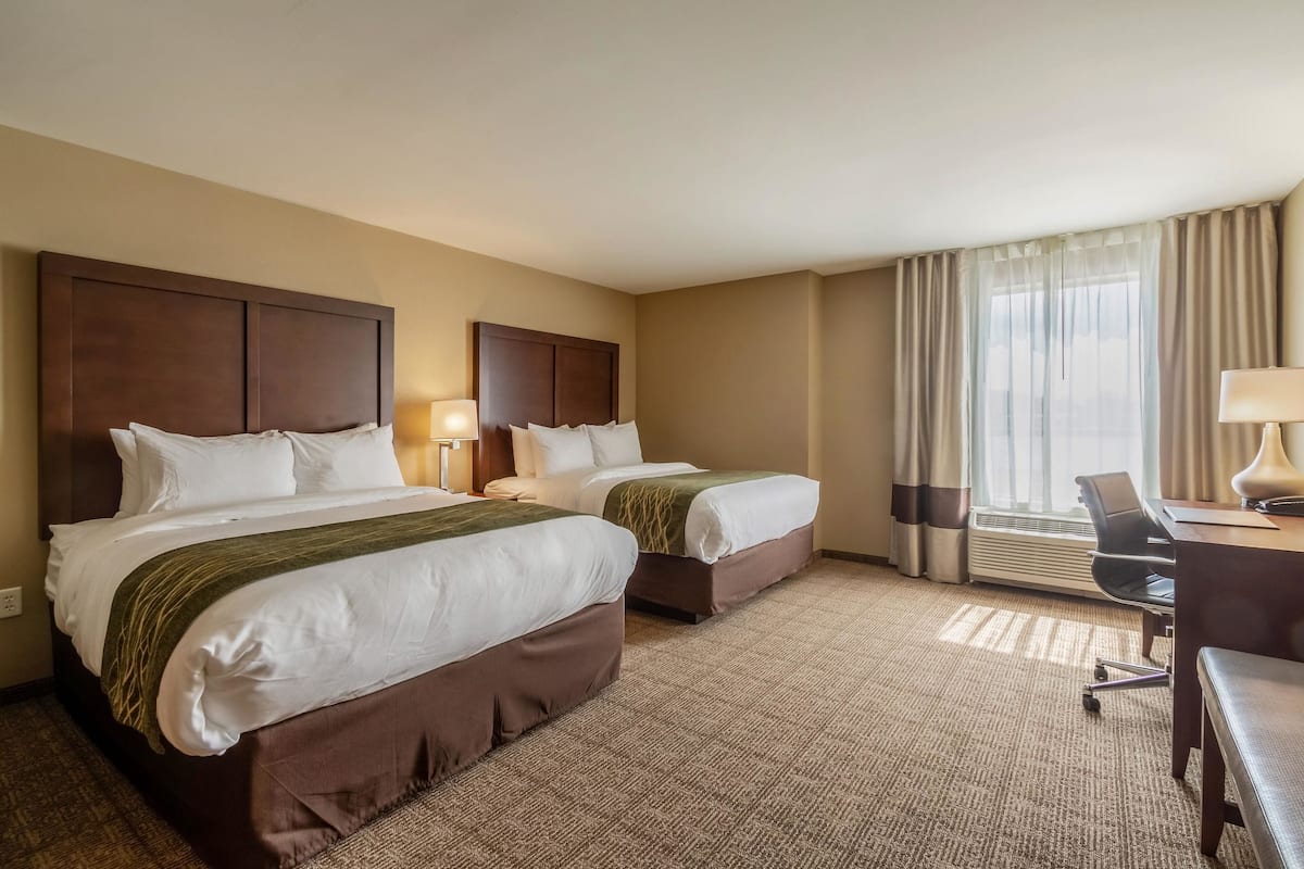 A hotel room with two beds, a desk, a chair, and a large window with curtains.