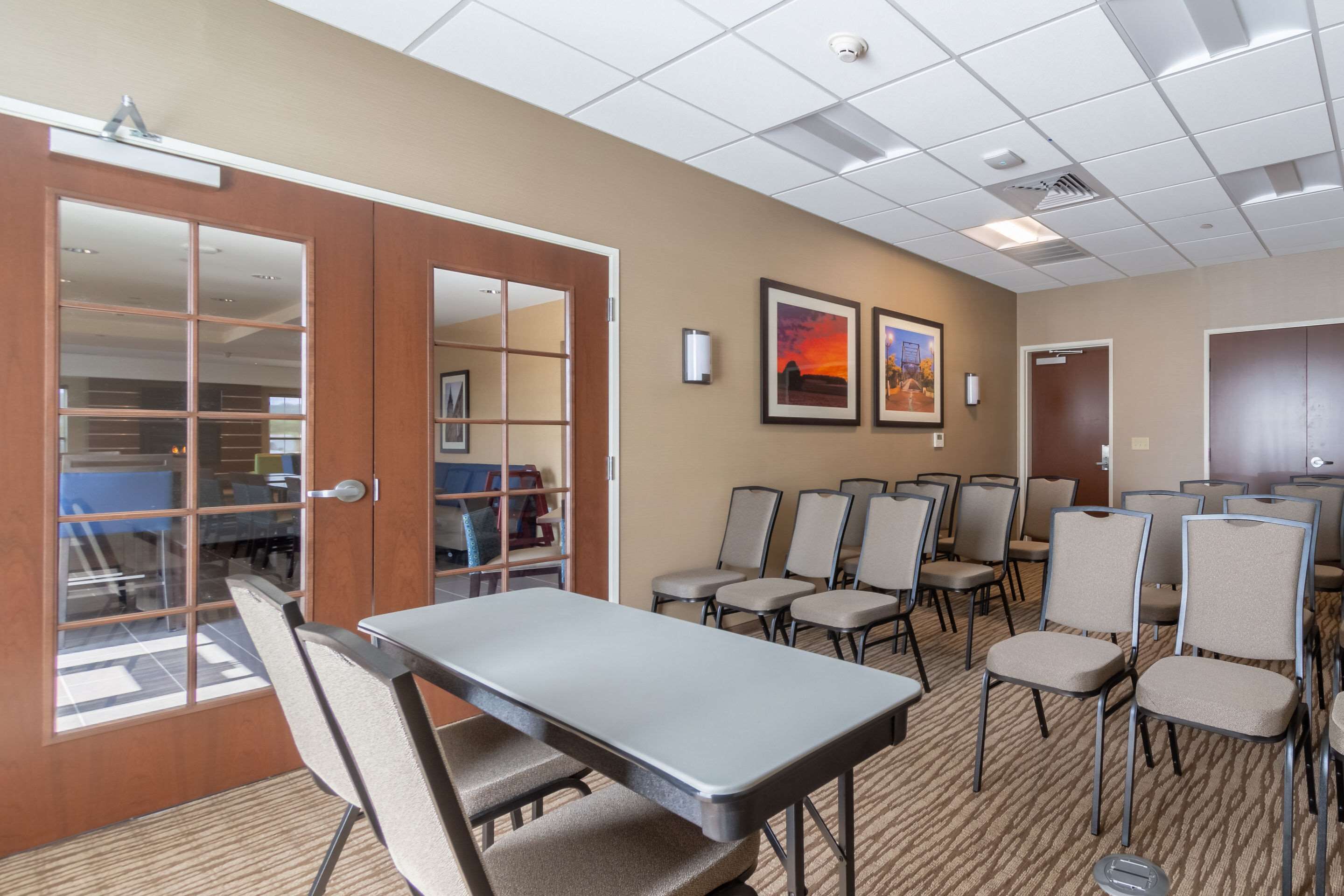 A conference room with a long table and multiple chairs, a door with a glass panel, and framed pictures on the wall.