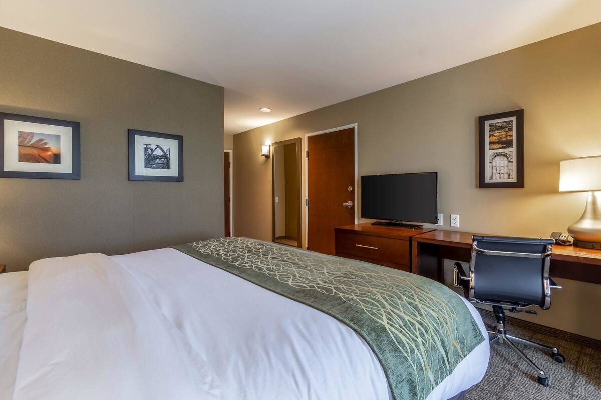 A hotel room with a large bed, a desk with a chair, a television, and framed pictures on the wall.