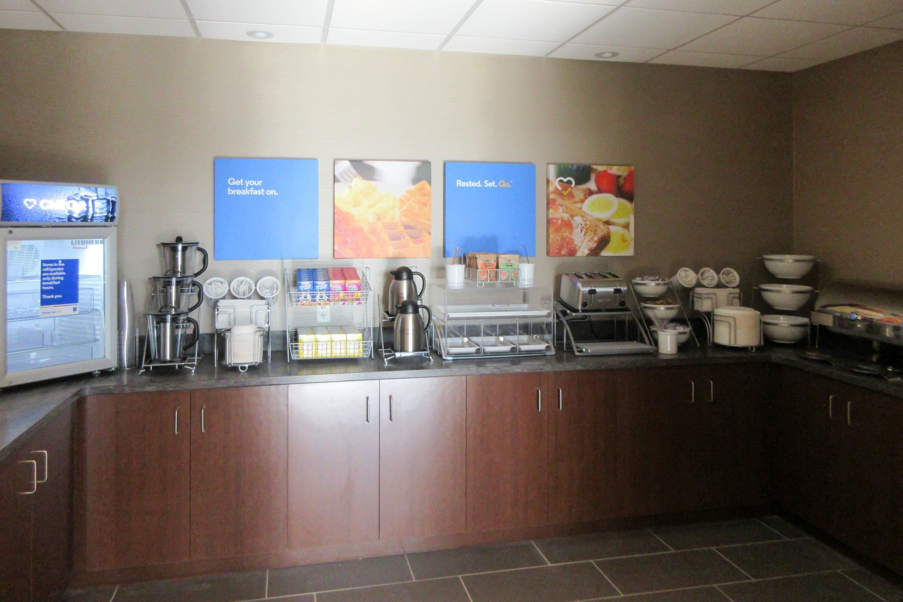 A breakfast bar with coffee makers, a kettle, and a refrigerator.