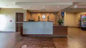 A hotel reception area with a stone wall, a reception desk, and a Coca-Cola refrigerator. - Comfort Inn & Suites – Harrisburg Airport – Hershey South (Middletown)