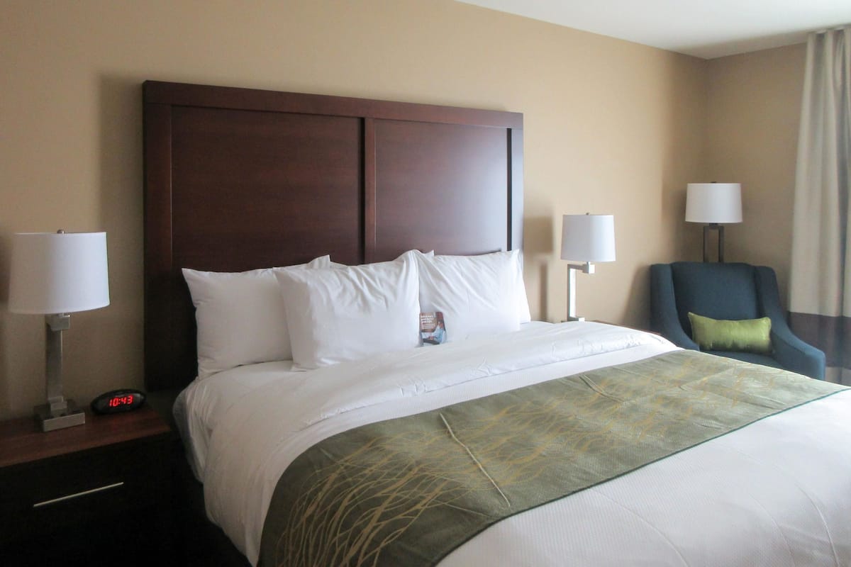 A hotel room with a large bed, two bedside tables with lamps, a chair, and a clock.