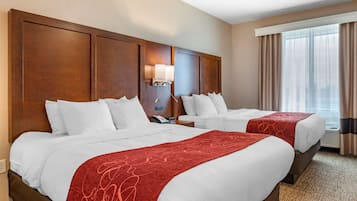 A hotel room with two beds, a wooden headboard, a bedside lamp, and a window with curtains.