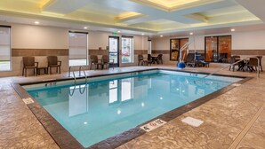 An indoor swimming pool with clear water, surrounded by seating areas and a ceiling with recessed lighting.