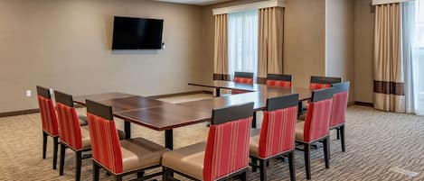A conference room with a large table and eight chairs, a flat-screen TV on the wall, and large windows with curtains.