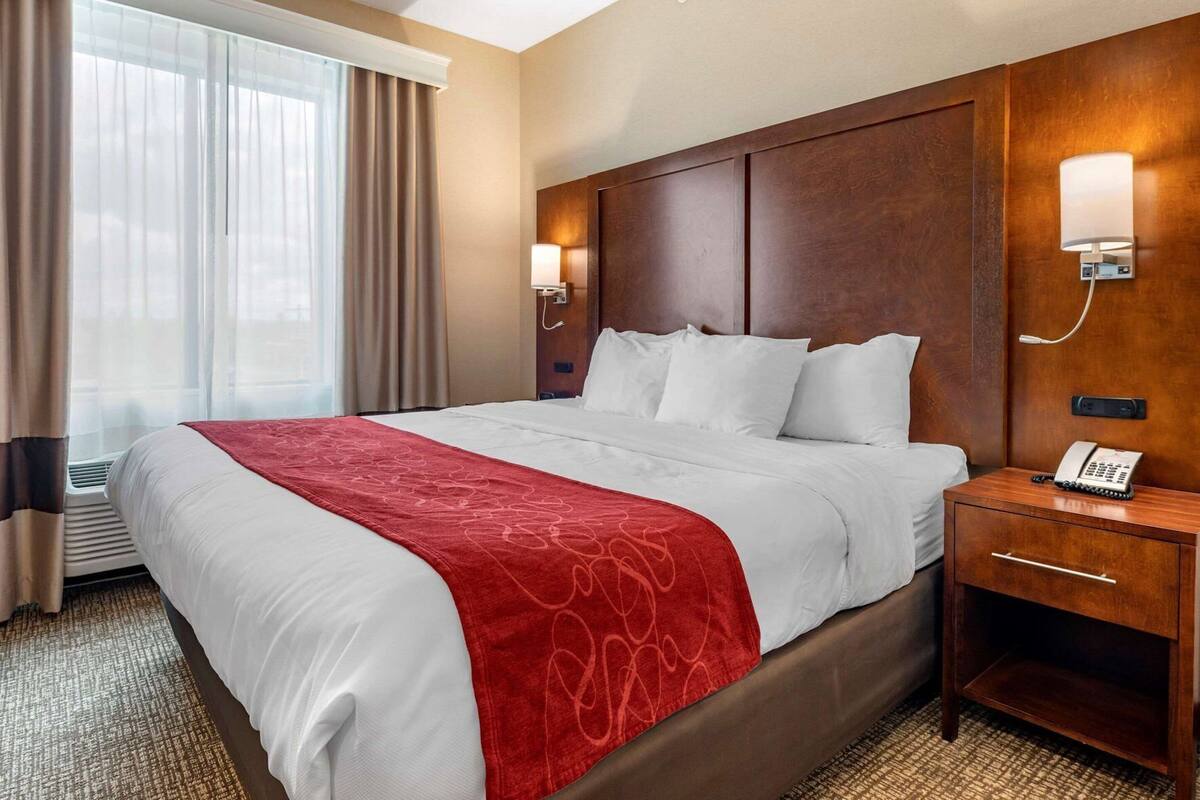 A hotel room with a large bed, a bedside table with a phone, and a wall-mounted light.