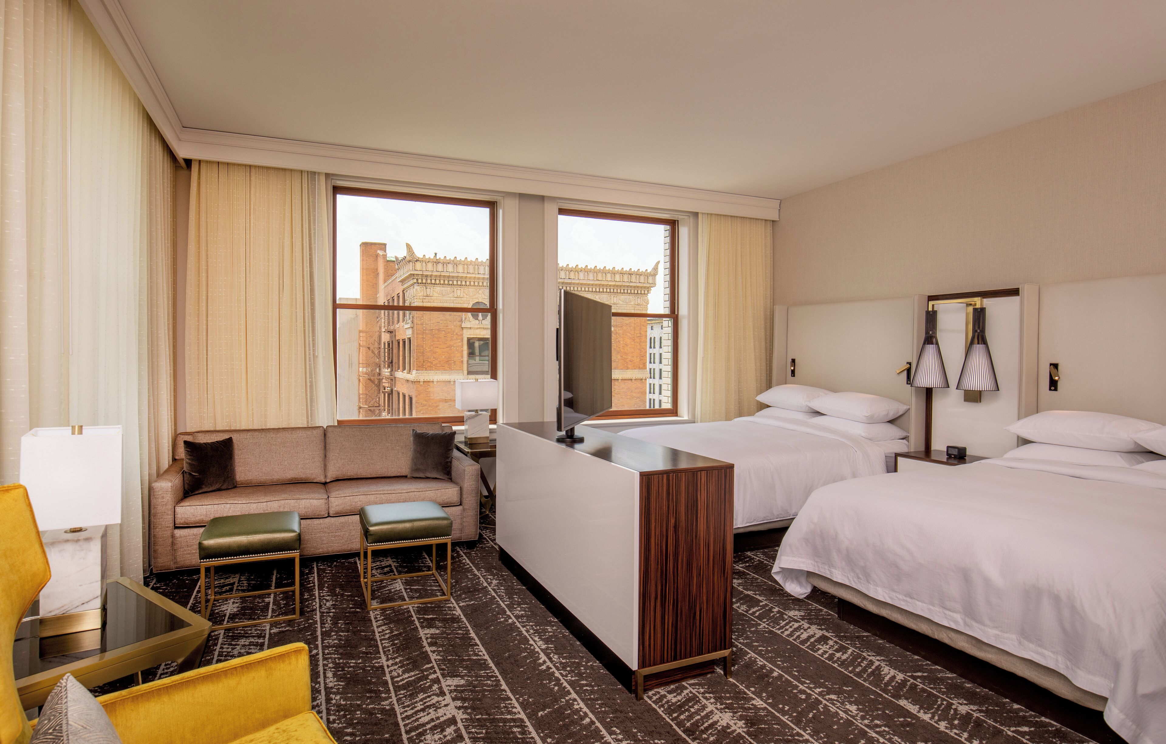Habitación de hotel con sofá, dos camas, escritorio y vistas a edificios.