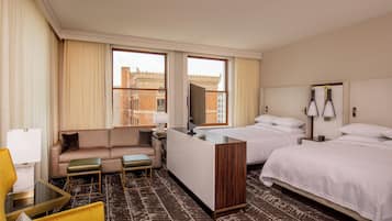 Habitación de hotel con sofá, dos camas, escritorio y vistas a edificios.