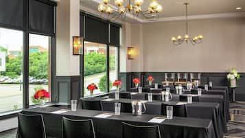 Una sala conferenze con tavoli apparecchiati per riunioni, ampie finestre con vista sul verde e un lampadario.