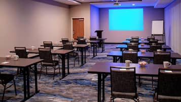 Un salón de conferencias con varias mesas y sillas, una pantalla de proyector y una pizarra.