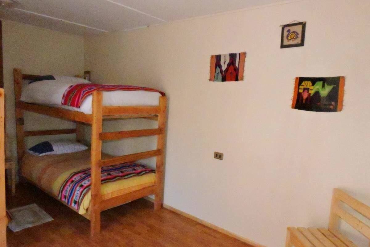 Une chambre avec un lit superposé, un plancher en bois, une petite chaise en bois et deux œuvres d’art encadrées accrochées au mur.