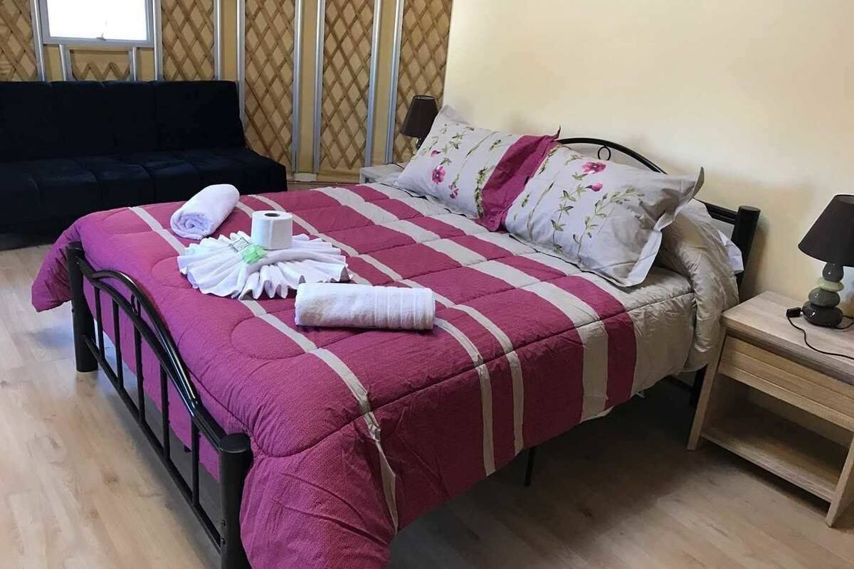 Un lit bien fait, avec une couvre-lit à rayures, un oreiller à motifs floraux et une table de chevet surmontée d’une lampe.