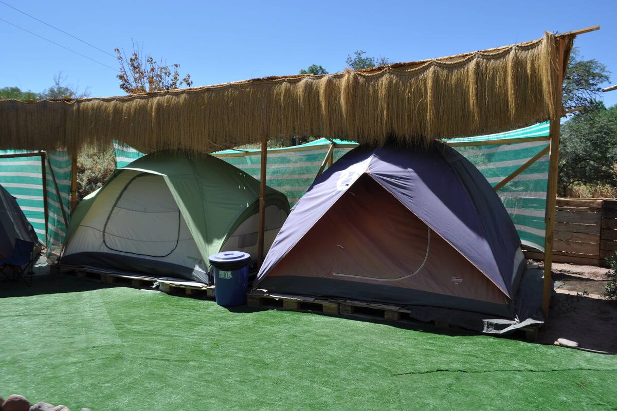 Deux tentes coiffées d’un toit de chaume, installées sur une surface verdoyante, avec une bâche rayée en arrière-plan.
