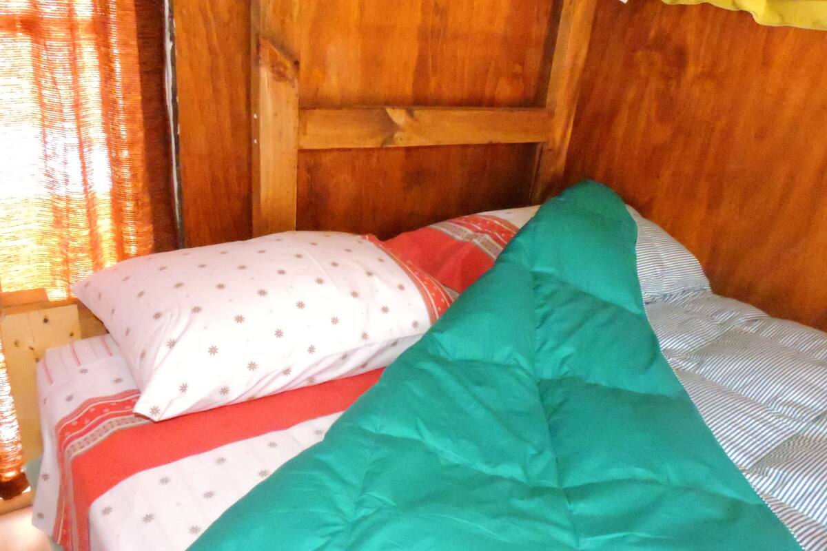 Un lit avec une couverture à rayures rouges et blanches, un oreiller vert et un oreiller blanc à motifs.
