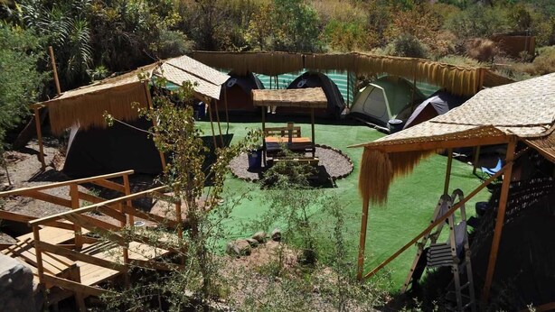 Ein Campingplatz mit mehreren Zelten, einem Picknicktisch und einer Holzbrücke.