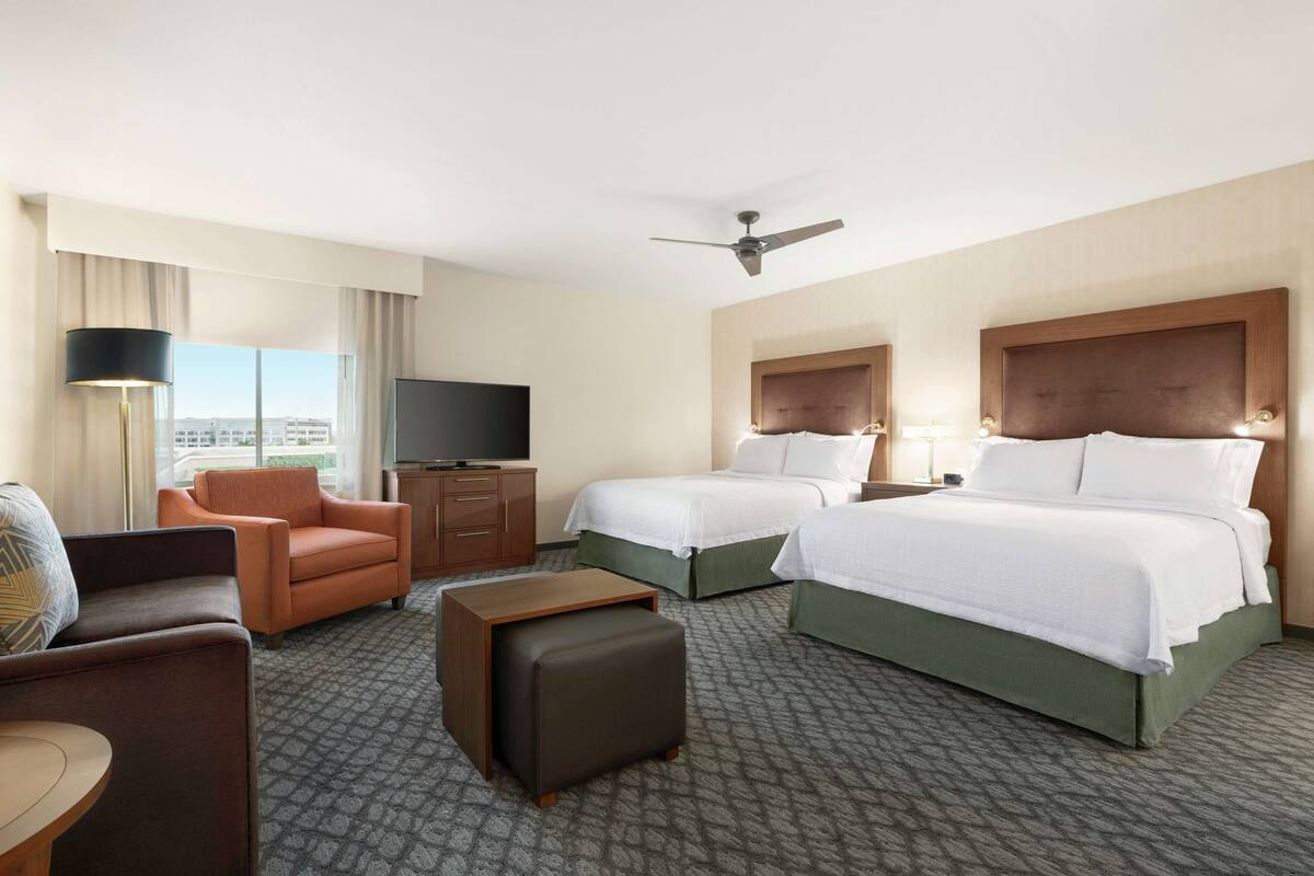 Habitación de hotel con dos camas, un sofá, televisión y vistas a la ciudad.