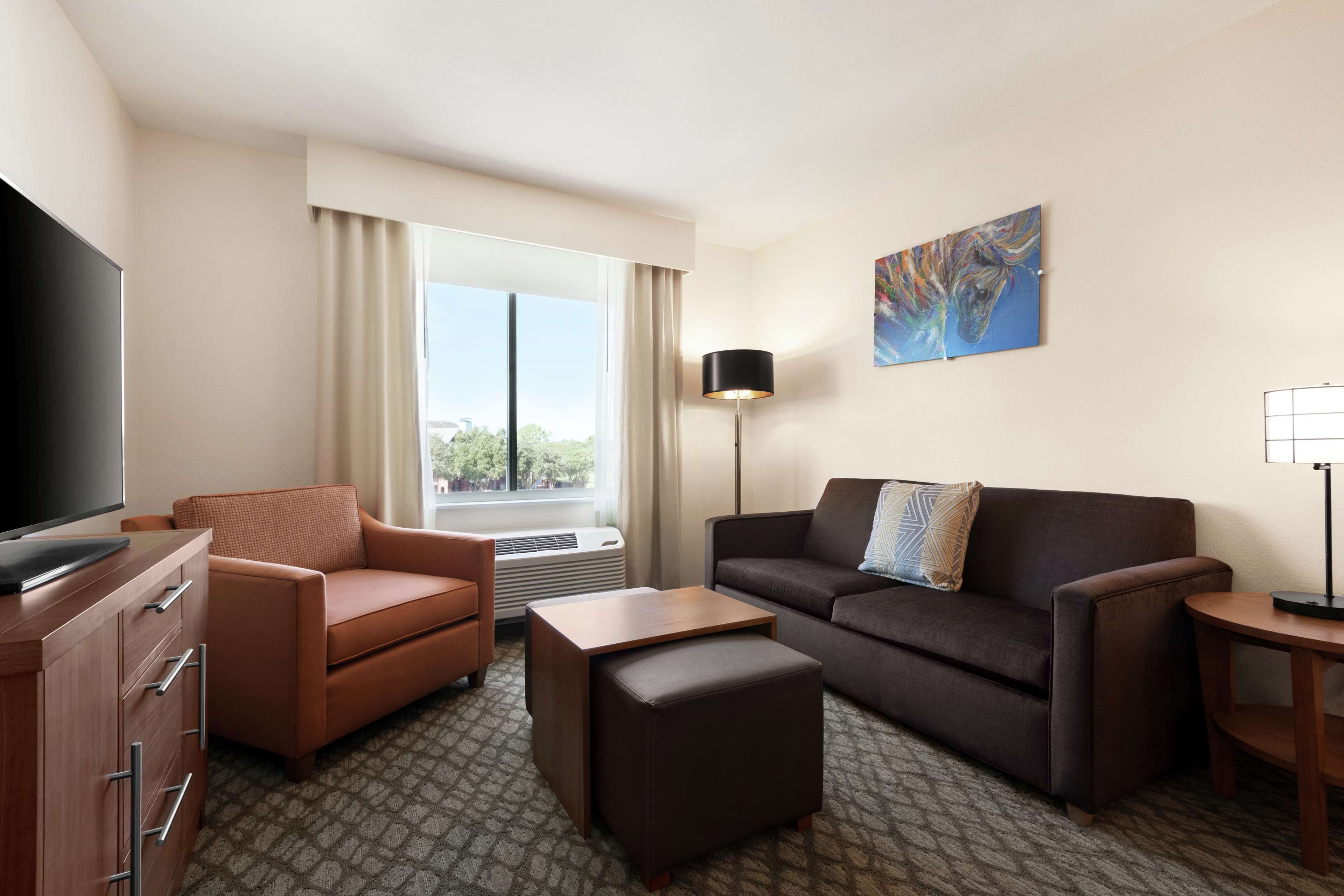 Een hotelkamer met een flatscreen televisie, twee banken, een salontafel, een lamp en een schilderij aan de muur.