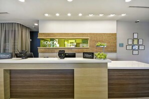 Um balcão de recepção moderno de hotel com um terminal de pagamento digital, uma placa com a inscrição "Hilton Honors" e uma placa com a inscrição "HOME2".