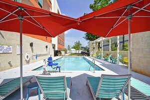 Zona de piscina con sombrillas rojas, sillas azules y señal de socorrista.