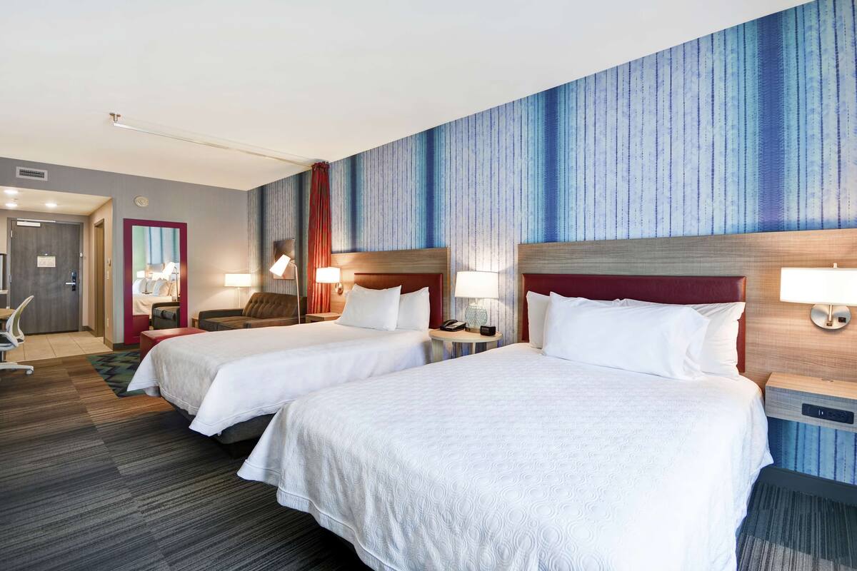 A hotel room with two beds, a desk, a chair, and a large window.