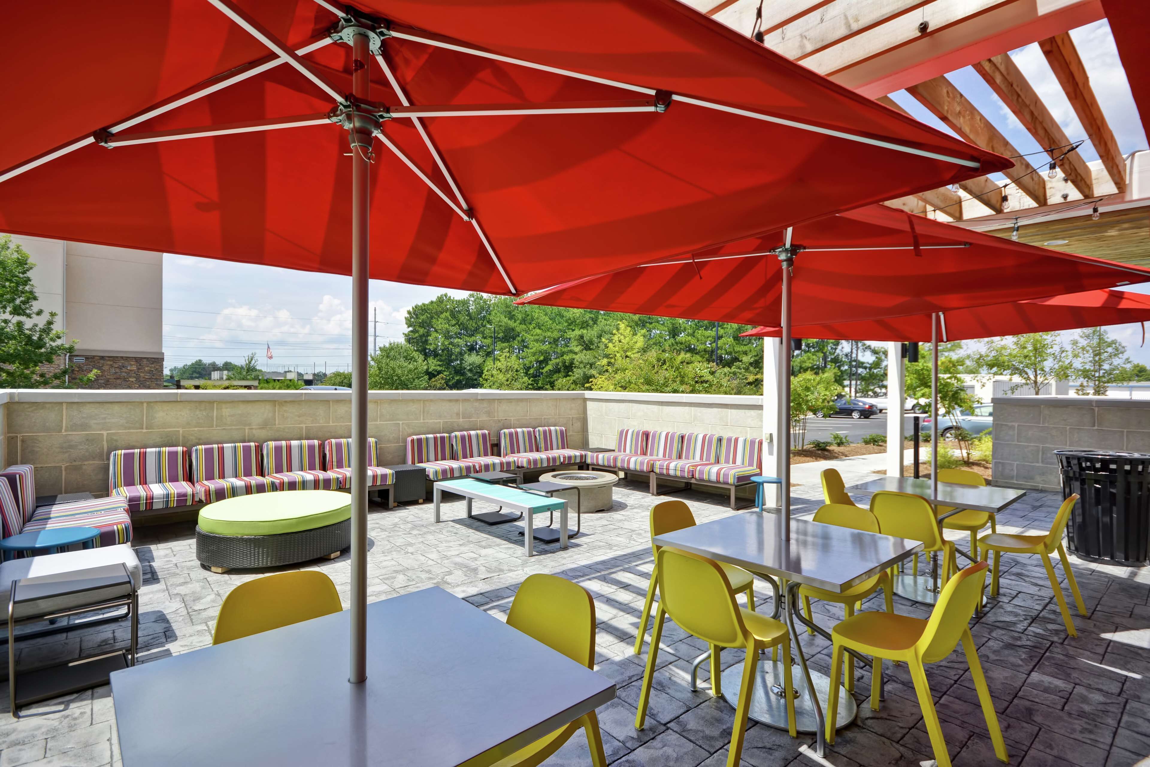 Une terrasse extérieure avec des parasols rouges, des chaises jaunes et des canapés à rayures.