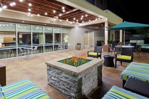 Área de terraço ao ar livre com lareira, assentos e uma seção coberta com mesas e cadeiras.