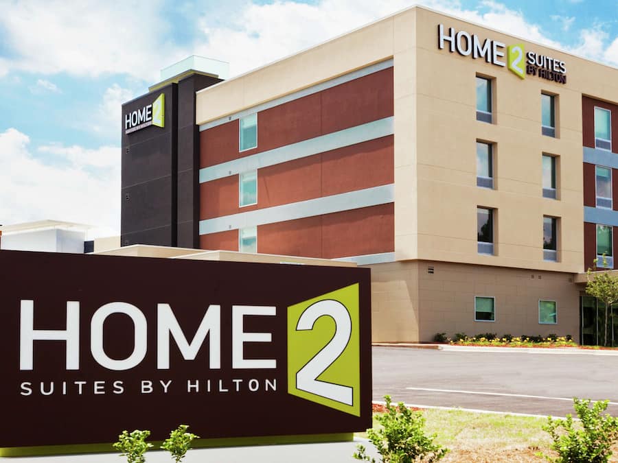 A hotel sign for Home 2 Suites by Hilton with a modern building in the background.
