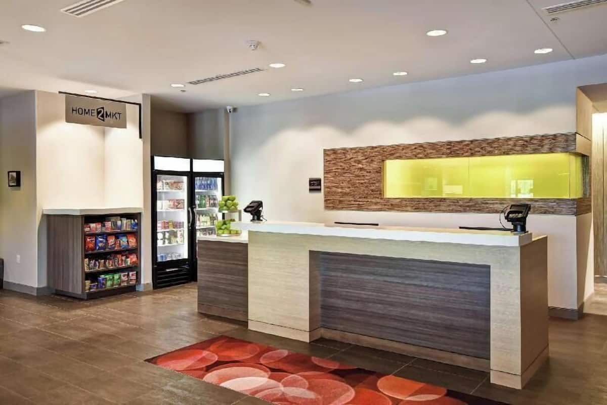 A reception desk with a modern design, a sign for 'HOME2MKT', and a self-service kiosk.